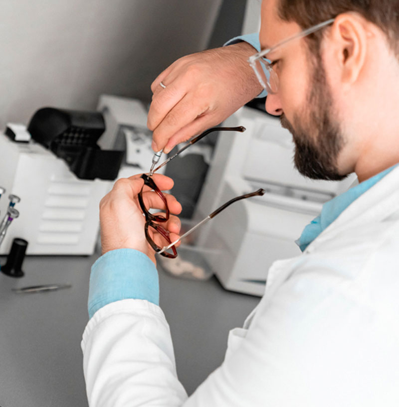 Fotografía de un hombre con bata blanca en un laboratorio, ajustando los tornillos de unas gafas con un pequeño destornillador